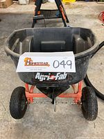 Front view showing black plastic hopper, Agri-Fab label, red metal frame, and two large wheels.