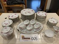Photo overview of the full set on a countertop including plates, bowls, cups, and serving pieces with floral cherry pattern and gold trim.