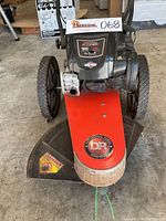 Front view of brush cutter showing wheels, engine cover label, and DR logo guard