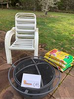 Photo showing fire pit, four white stacking chairs, and three bags of Miracle Gro potting mix on a patio.