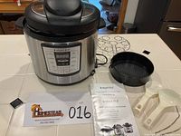 Wide shot displaying Instant Pot pressure cooker, cooking rack, black cooking pot, two plastic paddles, and user manuals on a table.