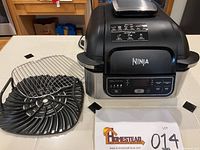 Ninja Foodi Grill main unit with removable grill plate and air crisp basket shown on a table.