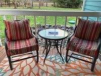 Front view of the two metal frame rocker chairs with striped cushions and the round glass-top metal frame side table between them on a porch.