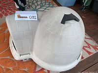 Side view of beige plastic igloo-shaped dog house with handle on top and an exterior brick pattern.