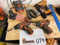 Photo of two Ridgid cordless drills, one with DeWalt bit attached, Craftsman stapler, Stanley Bostitch nailer, charger, and batteries on wooden table.