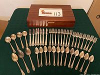 Photo showing full 42-piece flatware set laid out with wooden storage box on green cloth background.