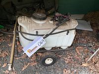 Front angled view of the white plastic tank mounted on a black metal frame with wheels, showing the filling cap and hose connections.