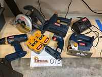 Overview photo showing the entire Ryobi cordless power tool set arranged on a concrete surface, including drill, circular saw, jigsaw, stapler, flashlight, two batteries, and charger.