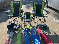 Photo showing two adult Seahawks quad chairs and one youth Seahawks quad chair with various folded camp chairs in carry bags placed in front.