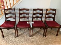 Full view of the four vintage wooden ladderback chairs in a row showing the dark wood finish, ladderback design, red upholstered seats, and curved legs.