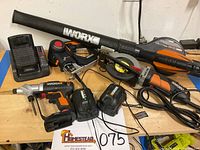 All tools arranged on a table: drill, saws, blower, trimmer, batteries, charger; showing all items included in the lot.