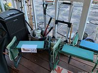 View of the lot showing three Besiter gardening benches, black patio trash receptacle, rolling cart with leaf rake and hand cart inside