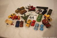 Overview photo of 22 miscellaneous diecast toy vehicles displayed on a white cloth background, showing various cars, trucks, tanks, and aircraft in different colors and conditions.