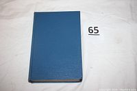 Closed view of the blue hardcover book, front cover facing up, showing texture and size relative to lot number marker.