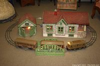 Full view of antique house and garage with electrified lights on, showing scale with train track and train pieces (not included).