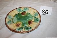 Full view of round ceramic plate with bamboo and leaf designs in green, brown and yellow glaze.