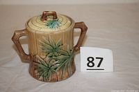Sugar container with lid on showing bamboo themed relief and two handles.
