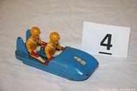 Front-side view of the blue cast iron bobsled toy with two figures seated wearing yellow helmets and uniforms.