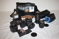 Full lot showing Konica FS-1 camera with 40mm lens, additional lenses, flash, teleconverter, filters, and black camera bag with tan bottom.