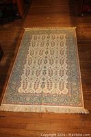Full view of rectangular hand-made oriental rug on wooden floor showing the overall design and fringes.