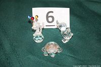 All three Swarovski crystal figurines displayed including the turtle, bird, and clown against a dark green cloth background with an evidence marker behind.