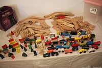 Photo showing both sets of wooden train tracks and a variety of wooden vehicles, including trains and cars, along with wooden road signs and trees arranged on a cloth surface.