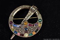 Front view of round Celtic brooch with various colored stones set in intricate metalwork.