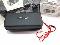 Two new black UCube protective storage cases with long red lanyard visible, closed, displaying the UCube logo on top, condition new.