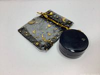 Photo of the jar of cream eye shadow and the black sheer gift bag decorated with gold moons and stars, showing size and presentation of the lot.