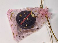 Blush compact inside pink sheer drawstring gift bag with gold stars and moon decoration.