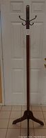 Full view of the 5.8 ft dark brown wooden coat rack stand with eight hooks and tripod base.