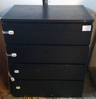 Front view of a black woodgrain dresser with four drawers featuring white child safety locks on each drawer.