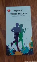 Front view of the Ngaolo Fitness Tracker white box packaging with silhouettes of a running man and woman along with brand and product name.