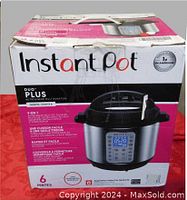 Box showing Instant Pot Duo Plus branding, capacity (6 pints/6 quarts), and features including easy one-touch cooking and secure locking lid. Box has visible dent.