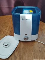 Front and side view of the blue and white Pure Guardian ultrasonic humidifier with lid removed and placed beside it on wooden surface.