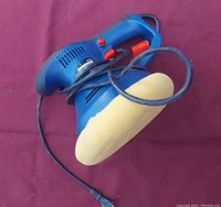 View of Simoniz blue polisher with attached beige foam polishing pad and power cord spread out on a maroon surface.