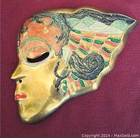 Front view of the solid brass mask showing detailed painted facial features and wing-like hair design.