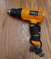 Side view of orange and black TackLife Pro heat gun with power cord coiled around handle showing overall condition and design.