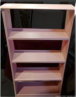 Front view of soft pink wooden bookshelf with four shelves, showing scuff marks and used condition.