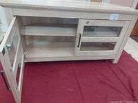 Front angle view of white woodgrain corner TV stand with one door open showing interior shelves.