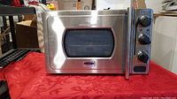 Front view of stainless steel Wolfgang Puck pressure oven with door closed showing control knobs and window.