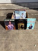 Vinyl albums in a cardboard box outdoors on pavement, featuring visible front covers of Dionne Warwick, Frank Sinatra, and Ray Charles albums.