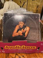 Photo of a cardboard box filled with vinyl LP albums featuring Anita Baker album cover on top showing significant wear.