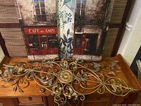 Ornate metal wall art piece on a wooden surface showing scrollwork and floral designs