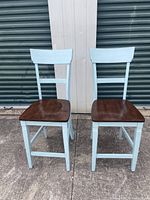 Front-facing view of two wooden bar stools with light blue frames and dark brown seats on concrete surface.