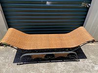 Bench full view showing curved woven rattan seat and black iron scrollwork base placed on outdoor surface.