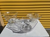 Photo of three small clear glass serving bowls and one large acrylic bowl with ladle on a white surface outside.