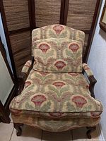 Front view of large accent armchair upholstered in red and gold floral print fabric with wooden arms and legs. Includes matching pillow.