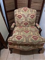 Front view of the large accent armchair showing the red and gold floral upholstery and wooden armrests and legs.