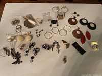 Photo of assortment of costume earrings laid out on table including sets in plastic packaging and loose pairs, showcasing a variety of styles and colors.